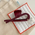 Detail of burgundy large hair claw clip with gold oval logo on minimalist fabric background - Angola Red