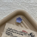Detaillierte Nahaufnahme einer mini Blumen-Haarklammer in Lila und Creme auf Tablett - Hellblau