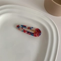 Detailed close-up of a colorful marble acetate duckbill hair clip on a white ceramic tray - Red Blue Marble Water Drop