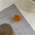Detail view of a translucent amber acetate hair claw clip on a gray textured surface - Brown