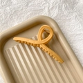 Detail of a large matte yellow shark hair claw clip on a textured beige tray - Matte Ginger
