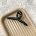 Détail d'une grande pince à cheveux noir mat sur un plateau texturé chic - Noir mat
