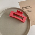 Close-up of a large matte coral pink rectangular claw clip on a minimalist gray tray - Matte Deep Pink
