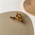 Dettaglio del mollettone in acetato maculato con molla in metallo su tappetino beige - Stampa Leopardata Scura