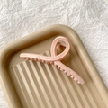 Détail d'une pince à cheveux rose torsadée au fini mat sur un plateau beige épuré - Rose Brillant