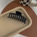 Detail showing the glossy black hair claw clip with multi-teeth design on a neutral tray - Glossy Black
