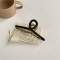 Dettaglio di un mollettone nero minimalista con denti in metallo dorato su tessuto beige - Nero Grande