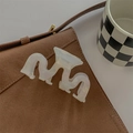 Detail shot of a large wavy pearl white acetate shark hair claw on a brown bag - White