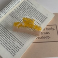 Detail van Koreaanse haarklem van acetaat in amber en beige op een open boek - Geel