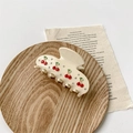 Detail view of cream hair claw with red rhinestone cherry pattern on a wooden tray - Cream