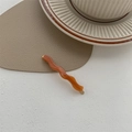 Detail view of wavy orange resin hair clip with golden metal base on a white table - Mocha Coffee