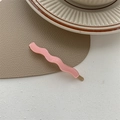Detailed top view of pink wave-shaped resin hair clip on a brown heart leather mat - Sakura Pink