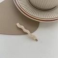 Close-up of wavy cream acetate hair clip with golden metal clasp on a textured surface - Milky White