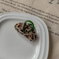 Détail d'une pince à cheveux écaille avec poignée vert foncé sur plat en céramique - Léopard Clair