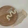 Dettaglio ravvicinato di una molletta per capelli ondulata beige con molla dorata - Onda Bianca