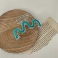 Dettaglio macro della molletta per capelli a onda verde trasparente su vassoio in legno - Onda Blu Chiaro