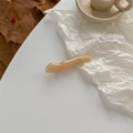 Gros plan d'une pince à cheveux ondulée en acrylique beige sur un fond blanc épuré - Abricot Clair
