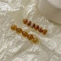 Close-up of amber tortoiseshell hair clips with round and heart beads on white paper - Caramel color