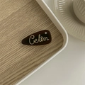 Detailed shot of a dark brown acetate hair clip featuring gold Celin lettering and rhinestone - Black Coffee