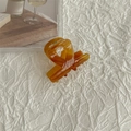 Dettaglio di una pinza per capelli in acetato ambrato con design a incrocio su tessuto bianco - Caramello
