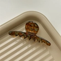 Close-up of elegant amber acetate hair claw clip with white brand logo lettering - Marbled Blue Brown
