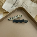Close-up of wavy acetate hair clips in black and spotted beige on a metal tray - Spot and Black
