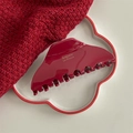 Dettaglio di una molletta per capelli bordeaux in acetato con scritte dorate su maglia rossa - Triangolo