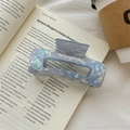 Detailansicht einer großen Perlmutt-Haarklammer mit Muscheltextur auf Vintage-Büchern - Metallblau