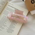 Macro view of a large translucent pink iridescent acetate hair claw clip on a book - Metallic Pink