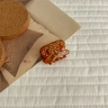 Detail view of large amber acetate hair claw clip with white dots on quilted background - Small Pretzel Shape