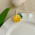 Détail d'une petite pince à cheveux ananas jaune sur une assiette en céramique blanche - Ananas