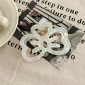 Detail of a large pearlescent white acrylic claw clip with an elegant hollow clover design - Iridescent White