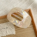 Detail of a beige iridescent hair claw clip with cutout design on a wooden tray - Iridescent Yellow