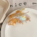 Detailed view of amber butterfly hair claw clip with pearlescent finish on a white plate - Rainbow