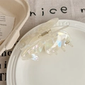 Detail view of pearlescent butterfly hair claw clip with golden logo on white ceramic plate - Pearl White