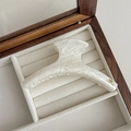 Close-up of cream acetate hair claw clip with golden YD logo in a wooden box - Cracked White