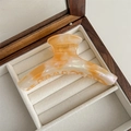 Detail of large acetate hair claw clip with amber texture in a wooden jewelry box - Orange