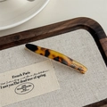 Dettaglio di fermaglio in acetato tartarugato con scritta dorata su vassoio in legno - Stampa Leopardata Scura