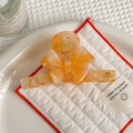 Detailaufnahme der orangefarbenen Haarklammer mit Goldschrift auf gestepptem Kissen - Orange