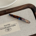 Detailed close-up of marble acetate hair barrette with gold logo on a wooden display tray - Lake Blue Coffee