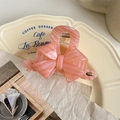 Detailed view of a pink bow hair claw with marble texture and gold logo on a tray - Pink Striped