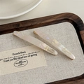 Detail of two acetate hair clips with gold lettering on a wooden display tray - Mermaid White (With Card)