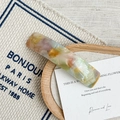 Detail of curved acetate hair clip with multicolored marble texture on a beige fabric - Rainbow
