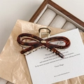 Detailed close-up of tortoise shell bow hair claw with gold spring and metallic accents - Amber