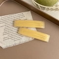Dettaglio di fermagli in acetato giallo con logo dorato su tessuto beige testurizzato - Stile Giallo Brillante Opaco
