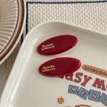 Détail de barrettes rouges rétro français avec lettrage doré sur un plateau décoré - Petite Forme Ovale