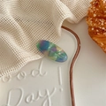 Macro shot of oval acetate hair clip with colorful marble texture and gold branding - Rainbow