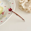 Detailaufnahme einer tiefroten Blumen-Haarklammer mit lila Perle auf cremigem Hintergrund - Lila Blume
