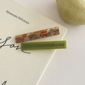 Nahaufnahme von bernstein- und olivgrünen Haarklammern aus Acetat auf einem Buch - Seeblau + Grün