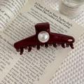 Detail shot of a dark red pearl hair claw clip with golden logo on a magazine backdrop - Oval Metal Logo (Wine Red) / Burgundy